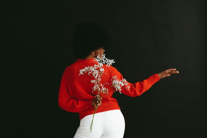 image-68 Back view of sensual black woman in white denim and white red sweater holding Gypsophila flower behind back posing on black backdrop