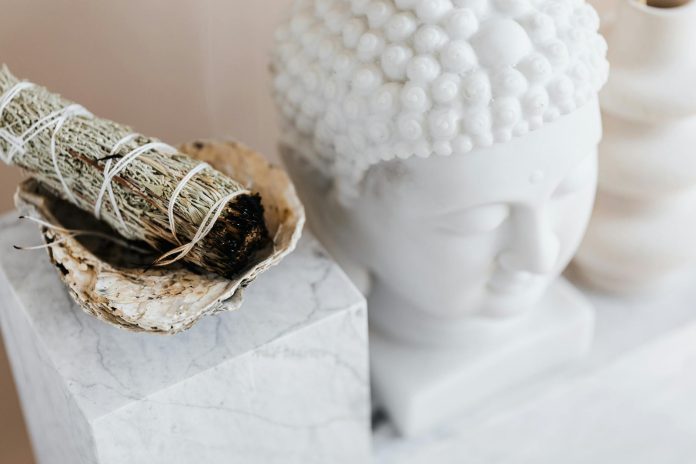 image-8 From above of sage candle in bowl placed on white marble shelf near plaster Buddha bust and creative shape vase for home decoration