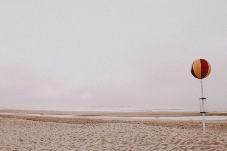 Colorful inflatable ball on metal pole placed on sandy seashore on cloudy day in summer