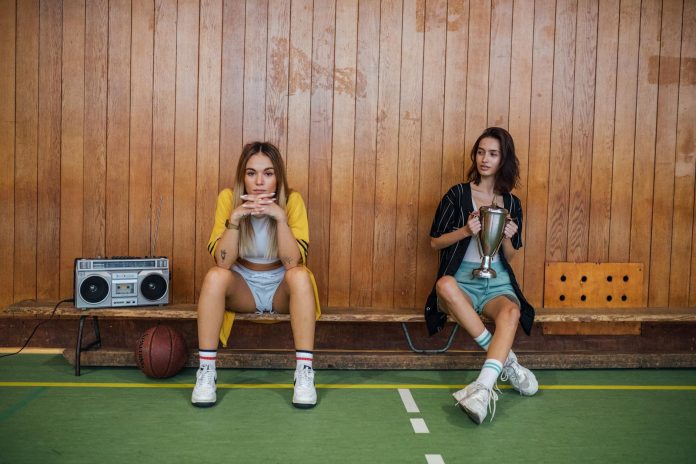 image-143 Two Women in Shorts and Long Shirts Sitting on a Bench at a Basketball Court
