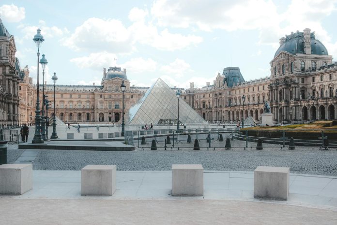Exterior of historic Louvre Museum build in Gothic style near famous landmark glass Pyramid located in center of Paris on summer day