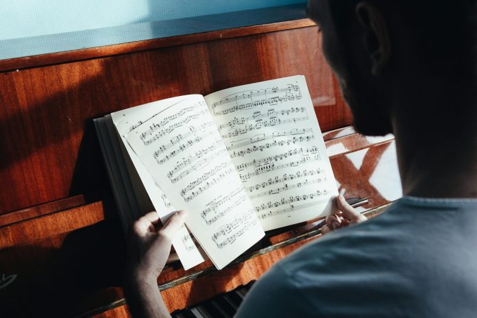 image-81 Back view of crop anonymous male pianist watching music paper with written notes near piano