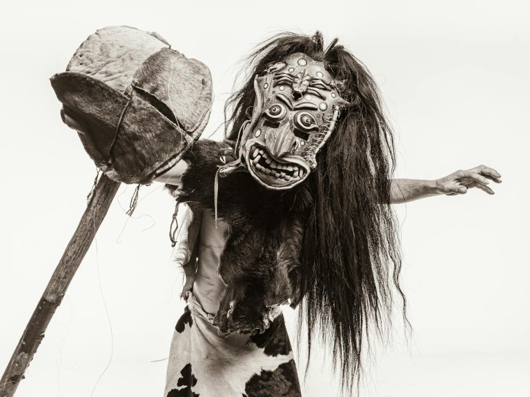 Sepia Toned Studio Shot of a Man in a Fur Carnival Costume and Mask with a Stick